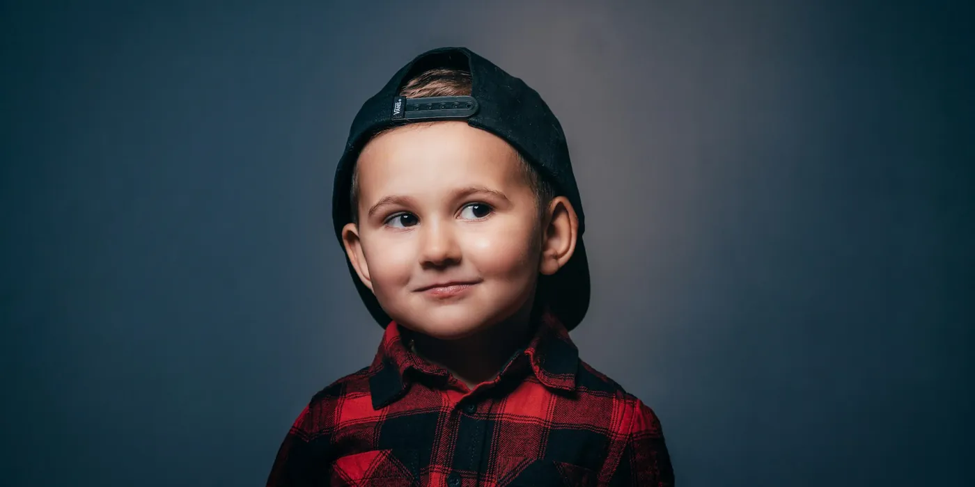 Smiling boy in a red plaid shirt and backwards cap on a deep blue backdrop