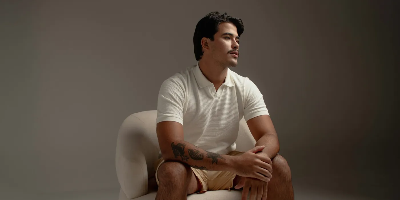 Man in a white knit polo and beige shorts seated in a curved white armchair