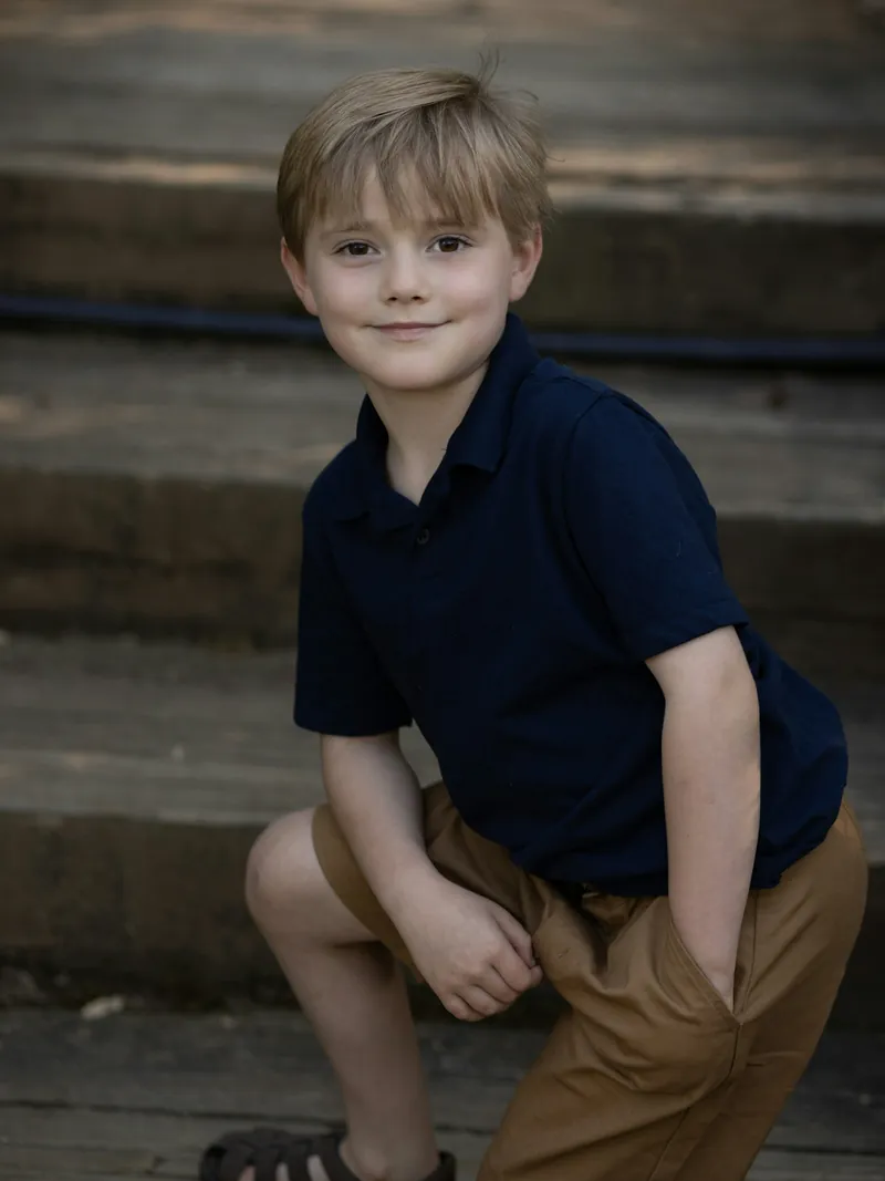 Boy crouching on garden steps in a navy short sleeve polo shirt