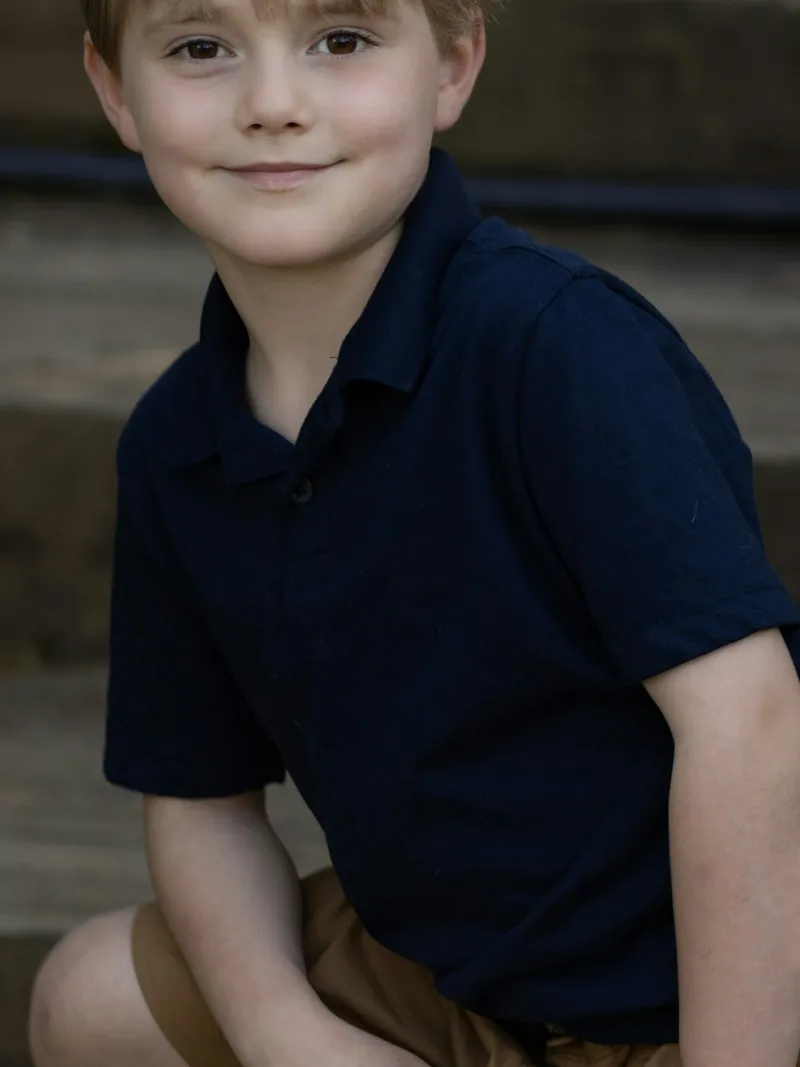 Boy crouching on garden steps in a navy short sleeve polo shirt