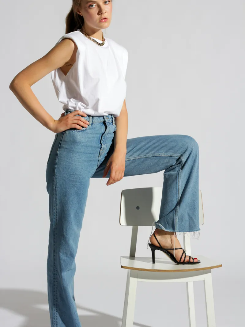 Model in mid wash high rise straight jeans with a white sleeveless top
