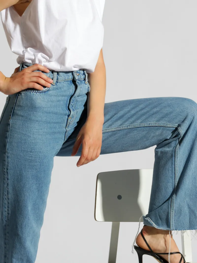 Model in mid wash high rise straight jeans with a white sleeveless top